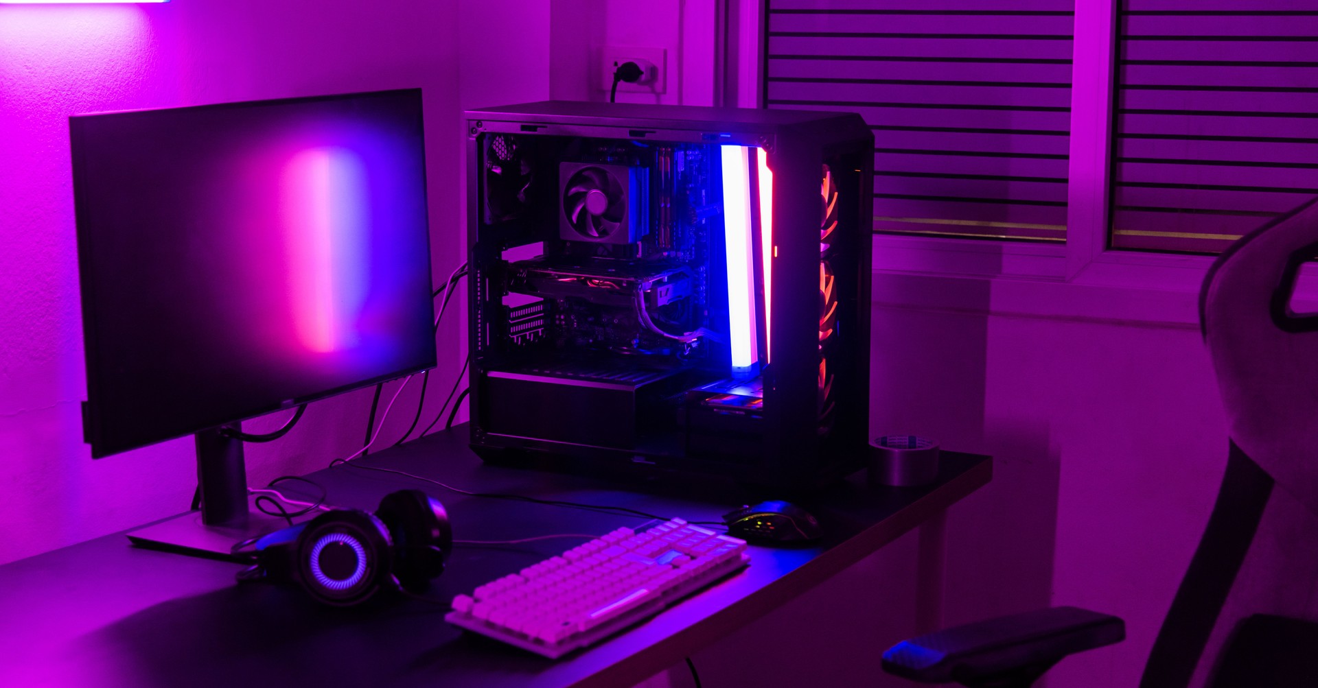A computer setup with a purple light dark background, games transmission modern equipment, modern gaming PC on desk with keyboard mouse monitor